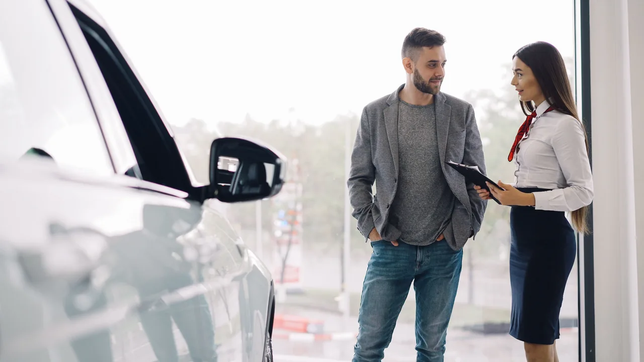 Un client et une conseillère discutent à côté d’une voiture blanche chez un concessionnaire.